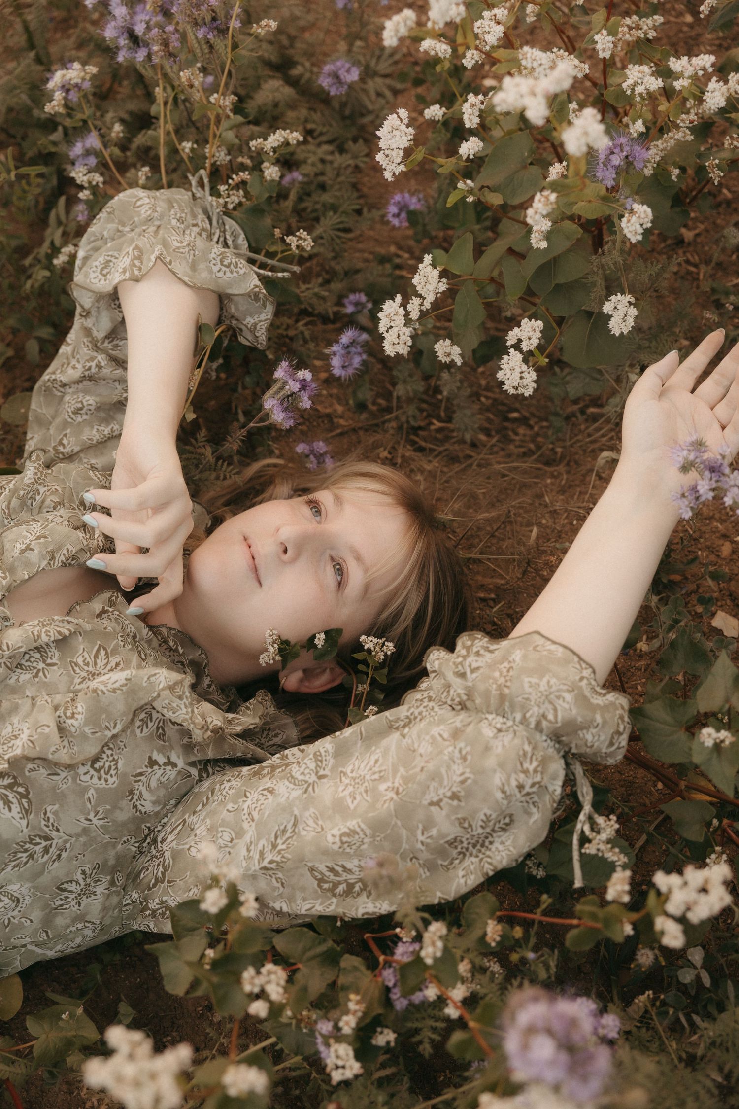 A person in a brown sweater poses with white flowers against a neutral background in a dreamy portrait setting.