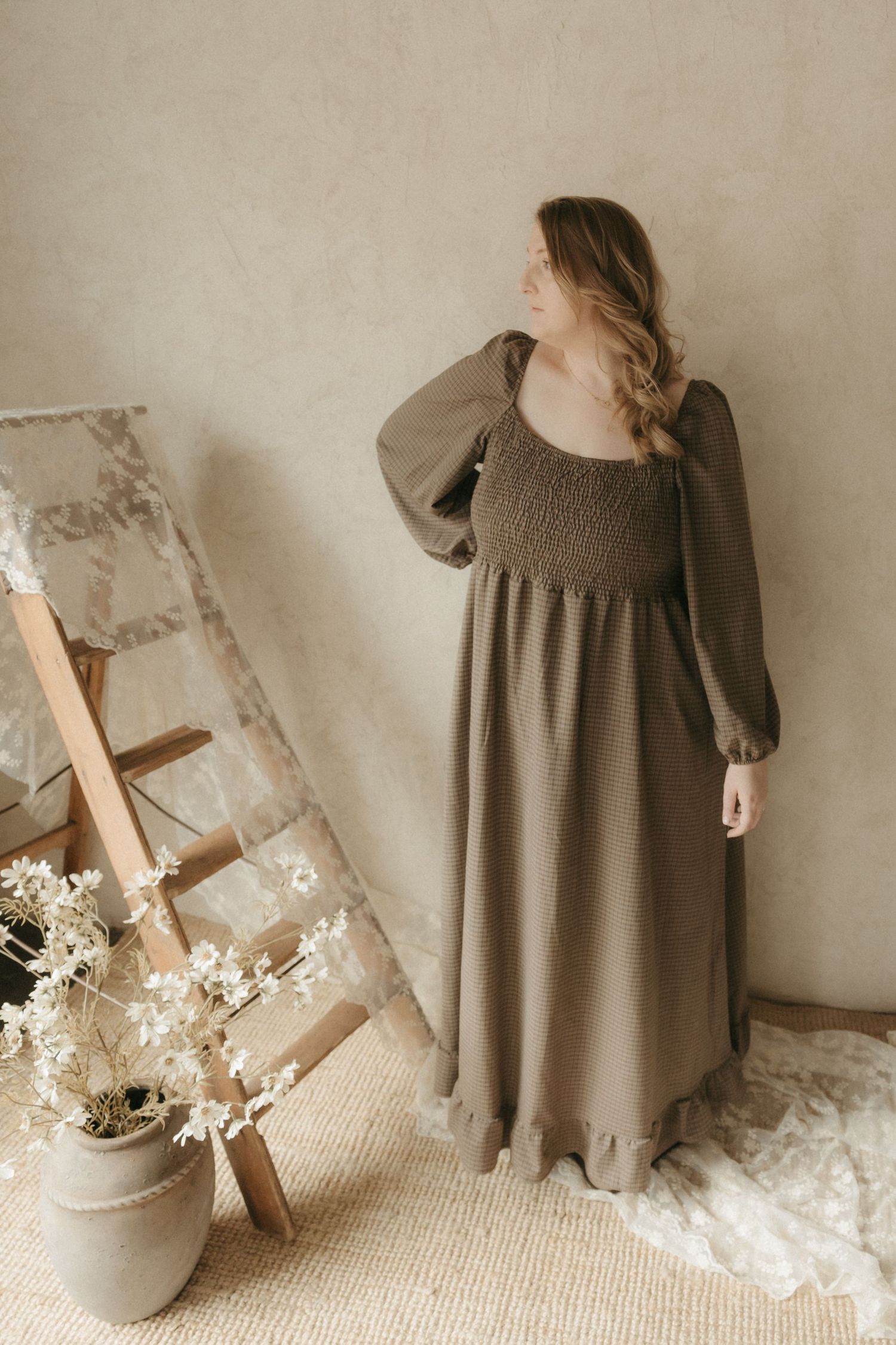 A person in a brown sweater poses with white flowers against a neutral background in a dreamy portrait setting.