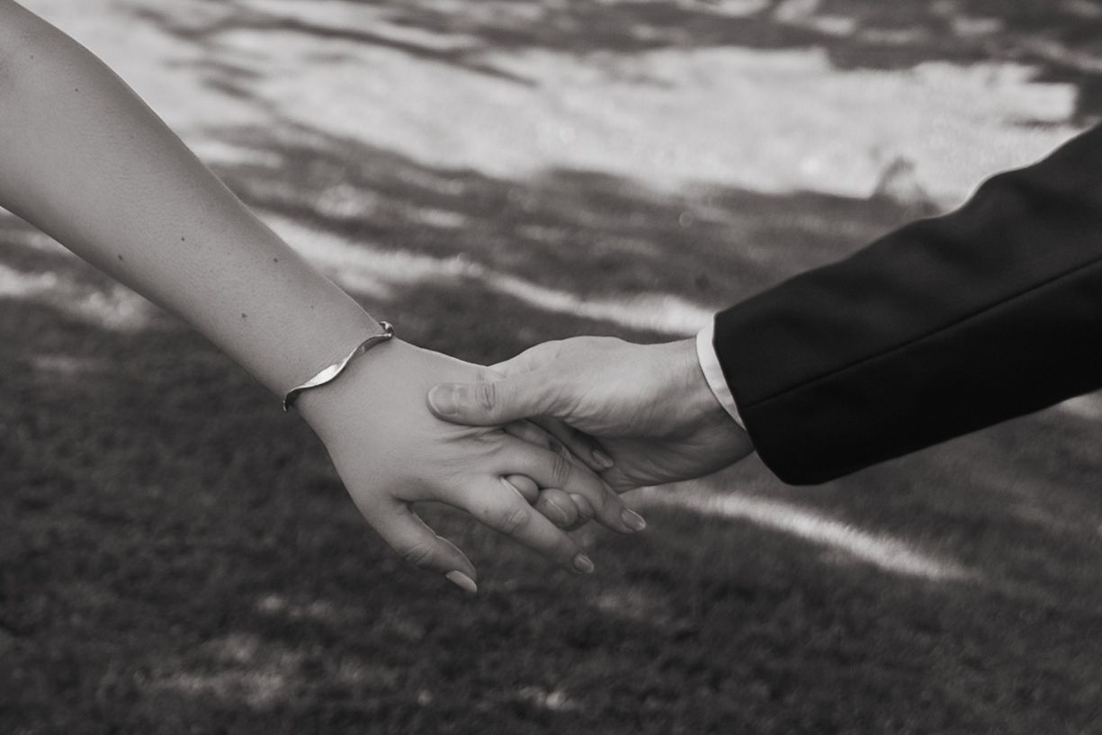Black and white close-up photo of two hands reaching toward each other against a blurred outdoor background.