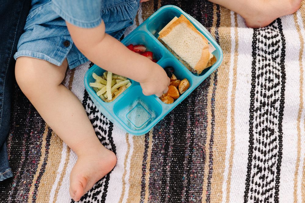 Small hands hold colorful toy blocks over a black and white patterned rug during playtime.