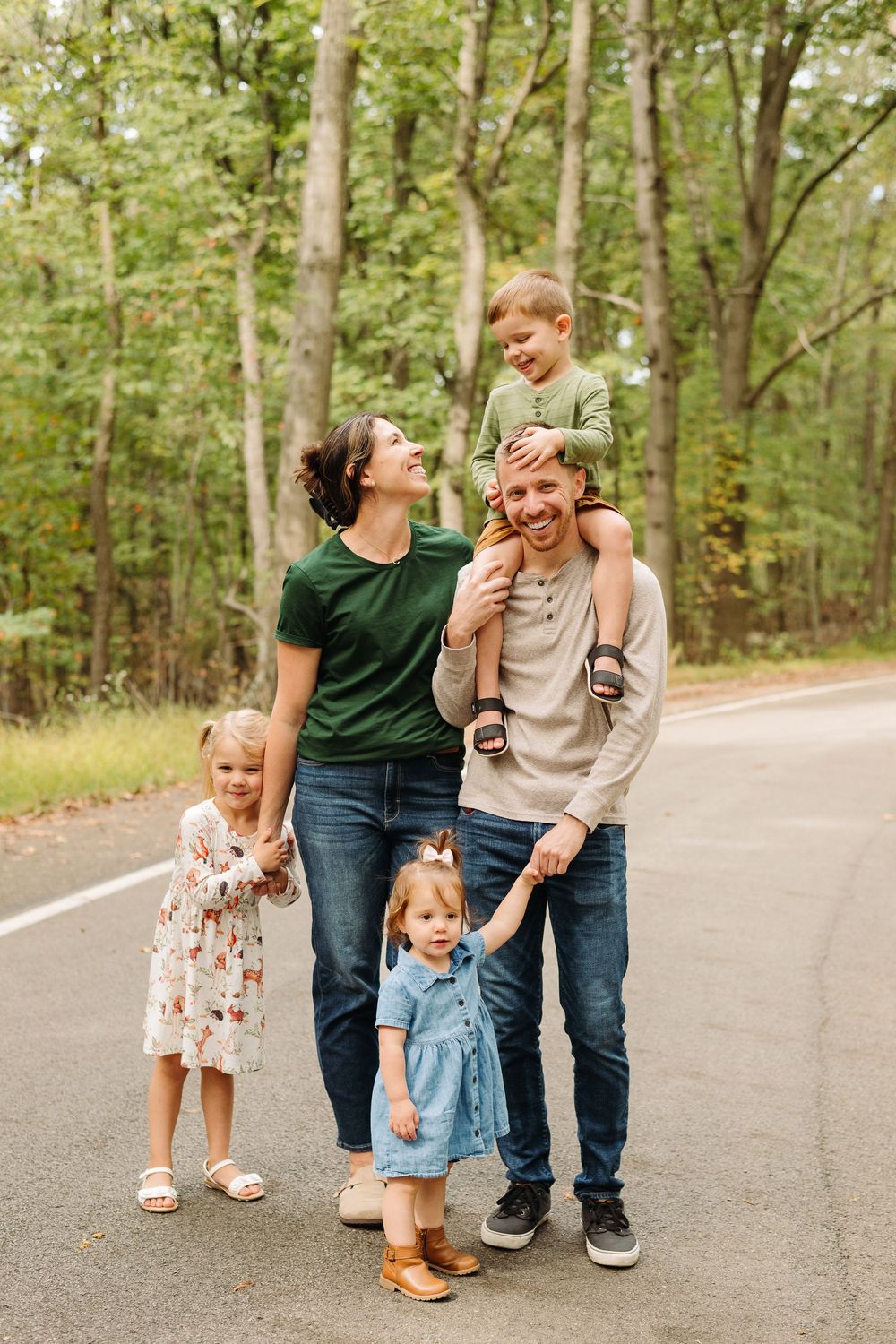 A playful family moment captured on a tree-lined road during an autumn photo session.