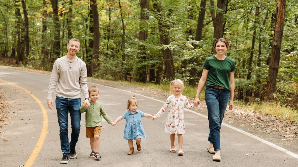 A panoramic sequence shows a family walking hand in hand down a tree-lined paved road on an autumn day.