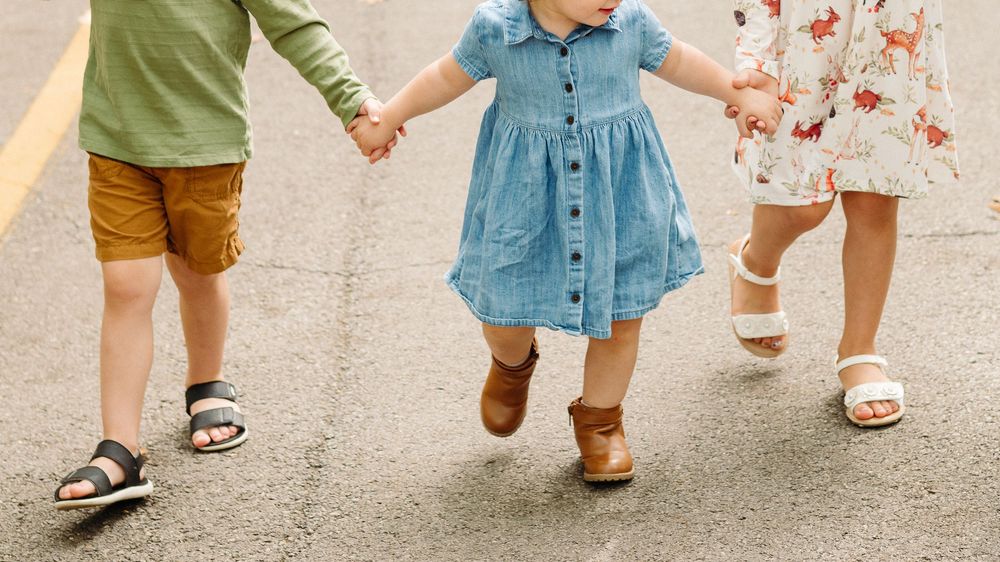 Row of children's legs and feet walking together on a sidewalk showing different styles of shoes and pants.