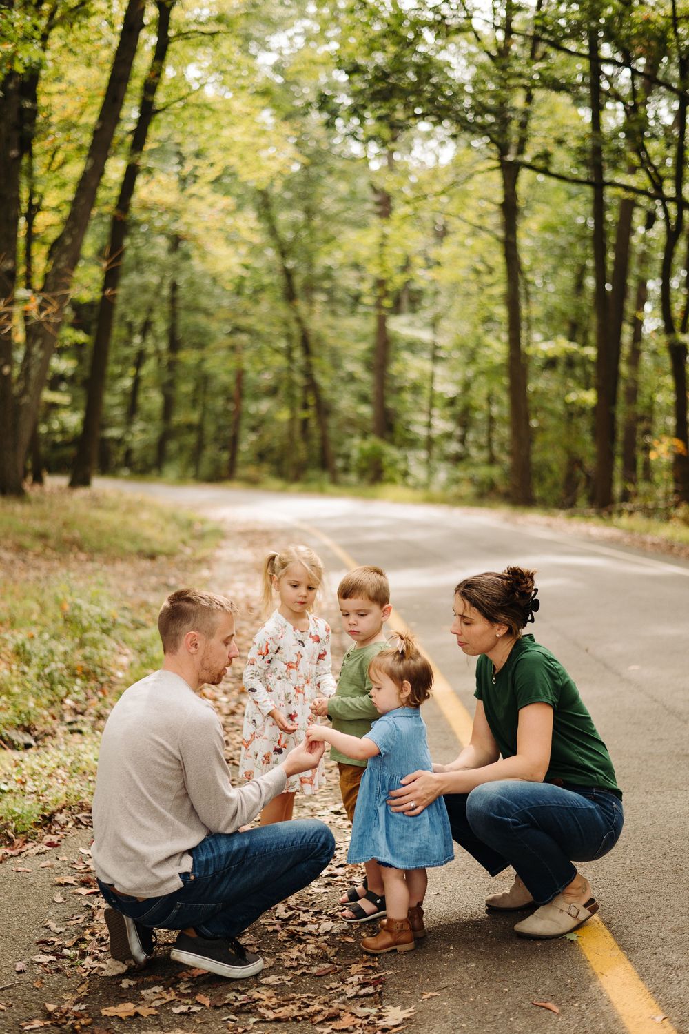 Candid family interaction on a wooded path with fallen leaves during a photo shoot.
