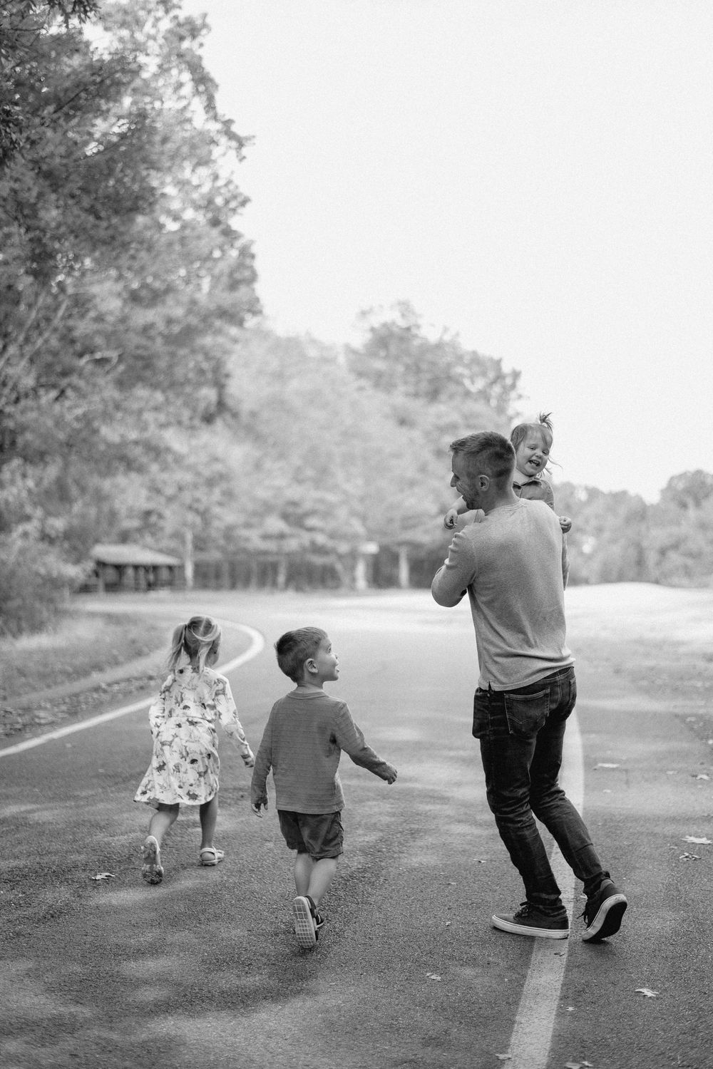 A black and white photo shows three people walking down a path together on a sunny day.