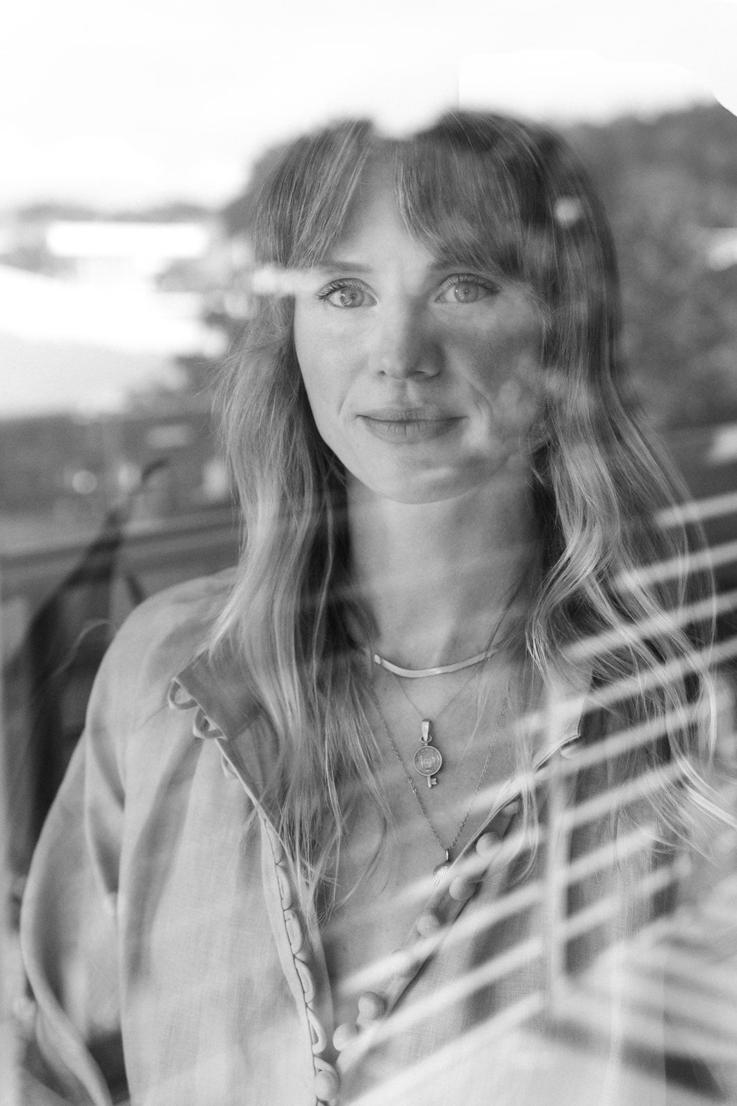 Black and white portrait through window blinds showing soft natural lighting and delicate features.