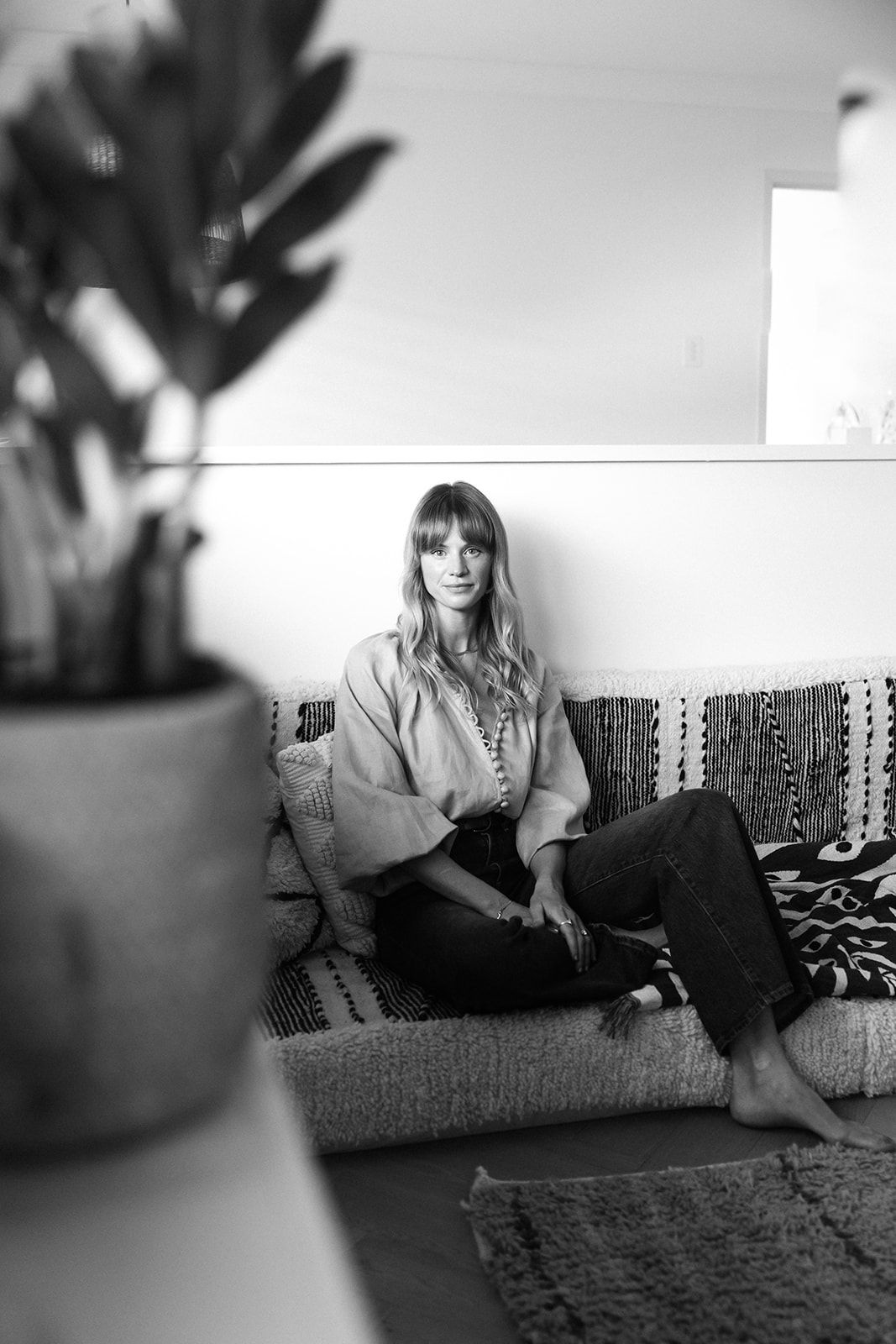Black and white indoor portrait of someone relaxing on a couch with a potted plant in the foreground.