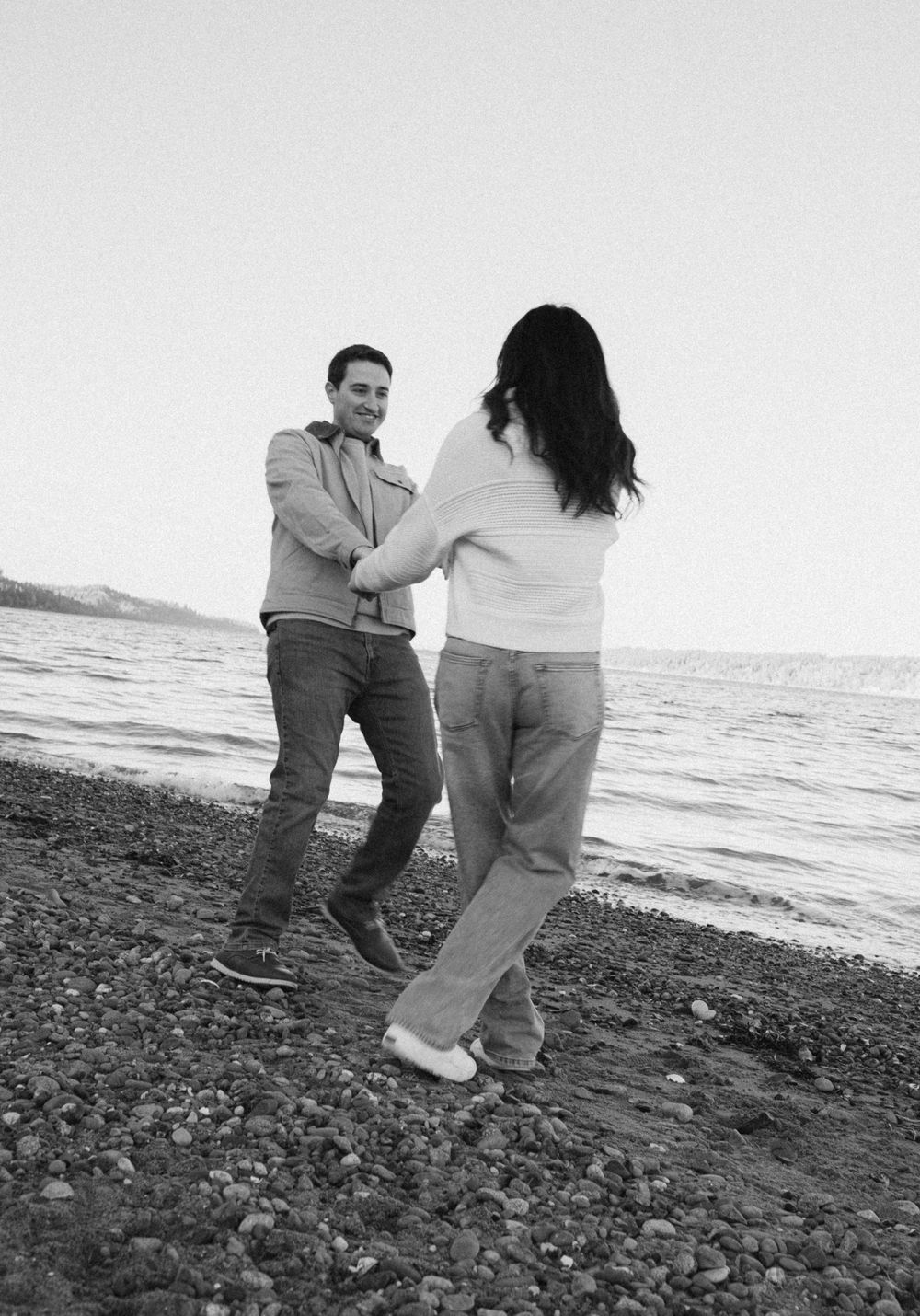 Black and white sequence of a couple walking and dancing on a rocky beach at sunset.