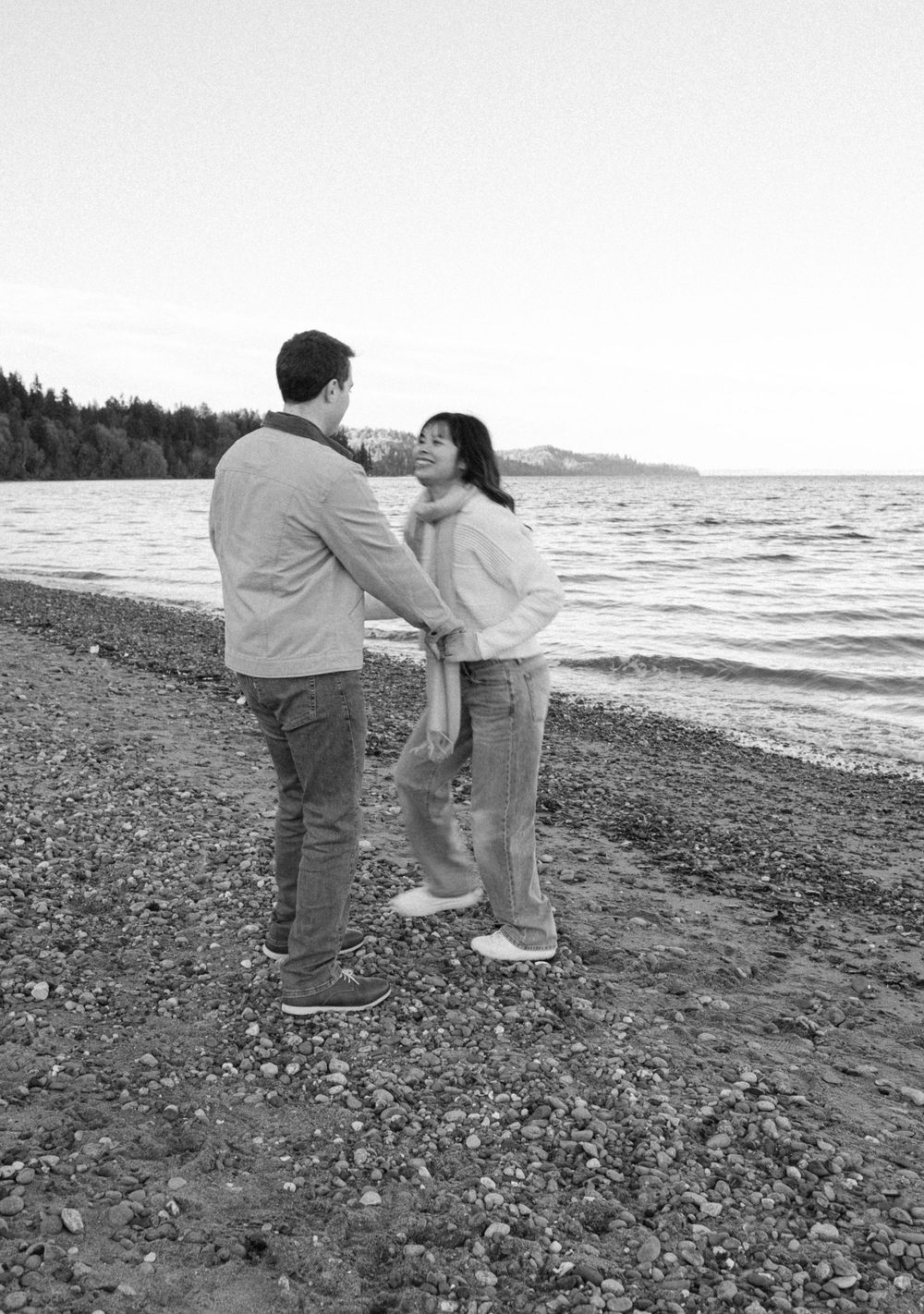 A sequence of black and white photos showing two people playing and interacting on a rocky beach shoreline.