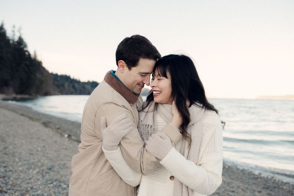 Couple in cream sweaters share intimate moment on rocky beach at sunset.