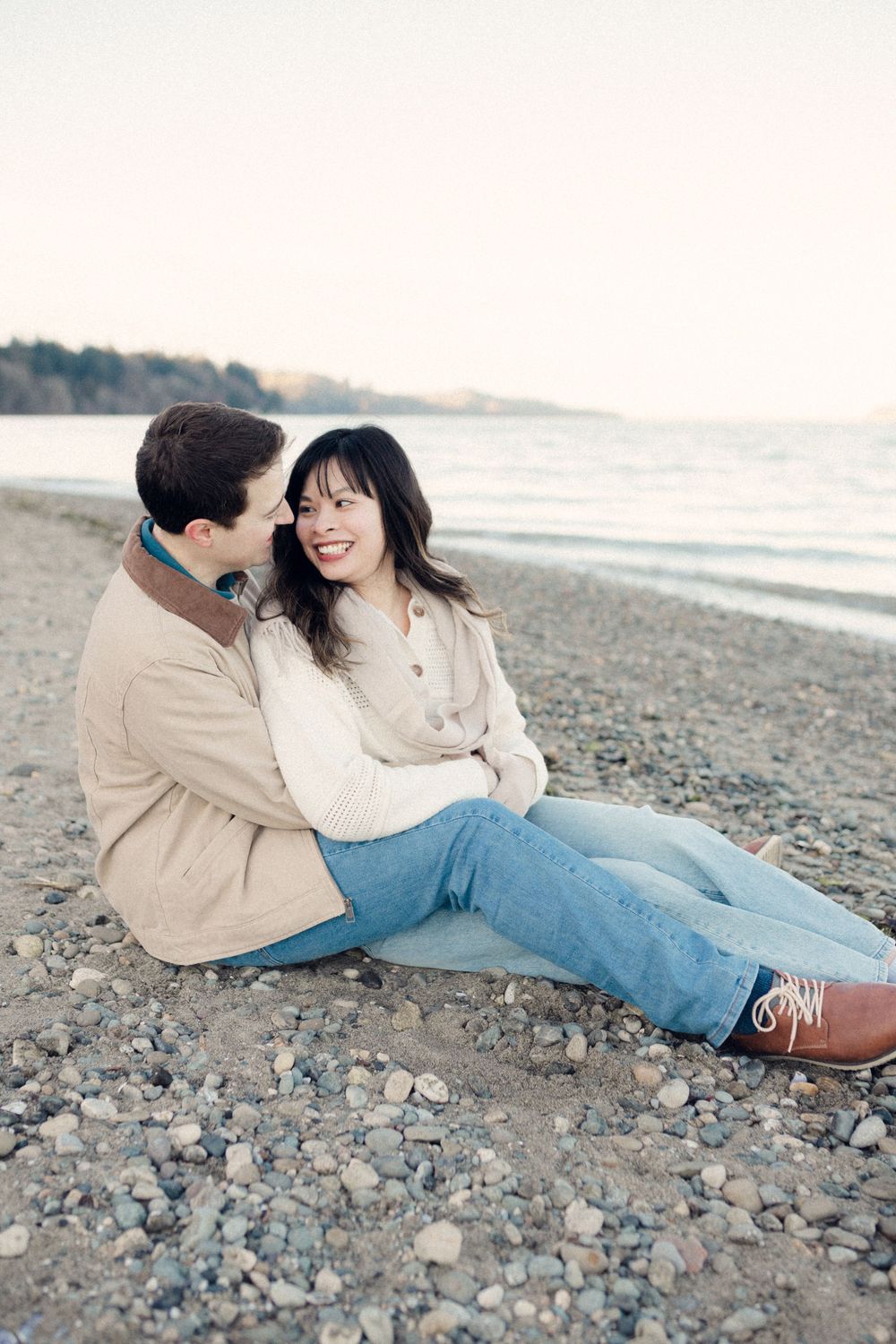 A couple lounges together on a rocky beach shore during golden hour.