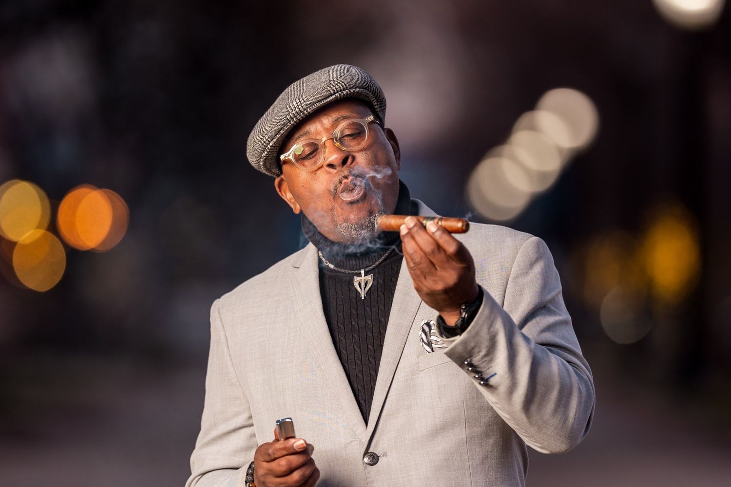 Close up of Randy Daye holding a cigar and blowing smoke while demonstrating proper cigar smoking technique.