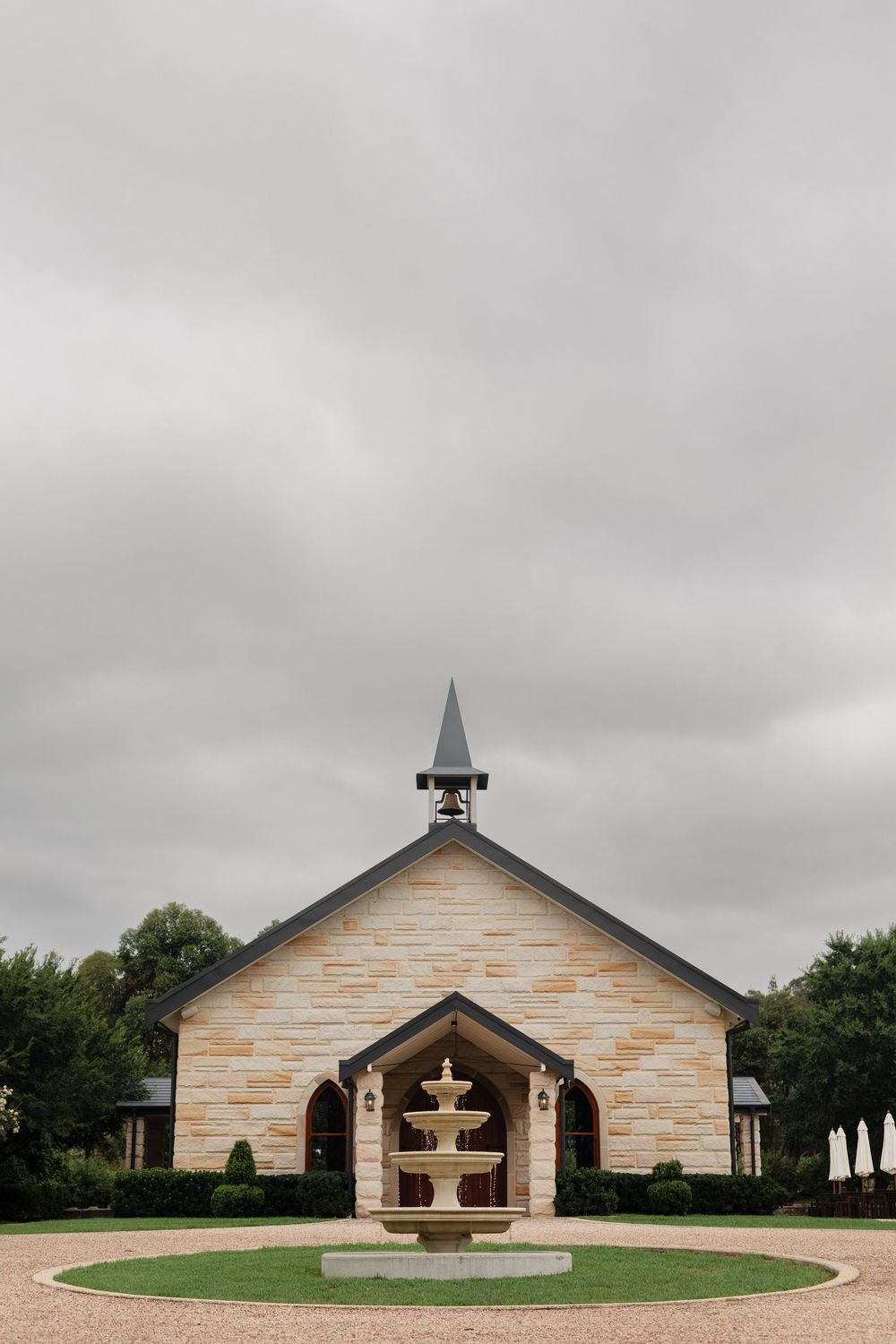 Modern stone church building with pitched roof and cross under cloudy sky.