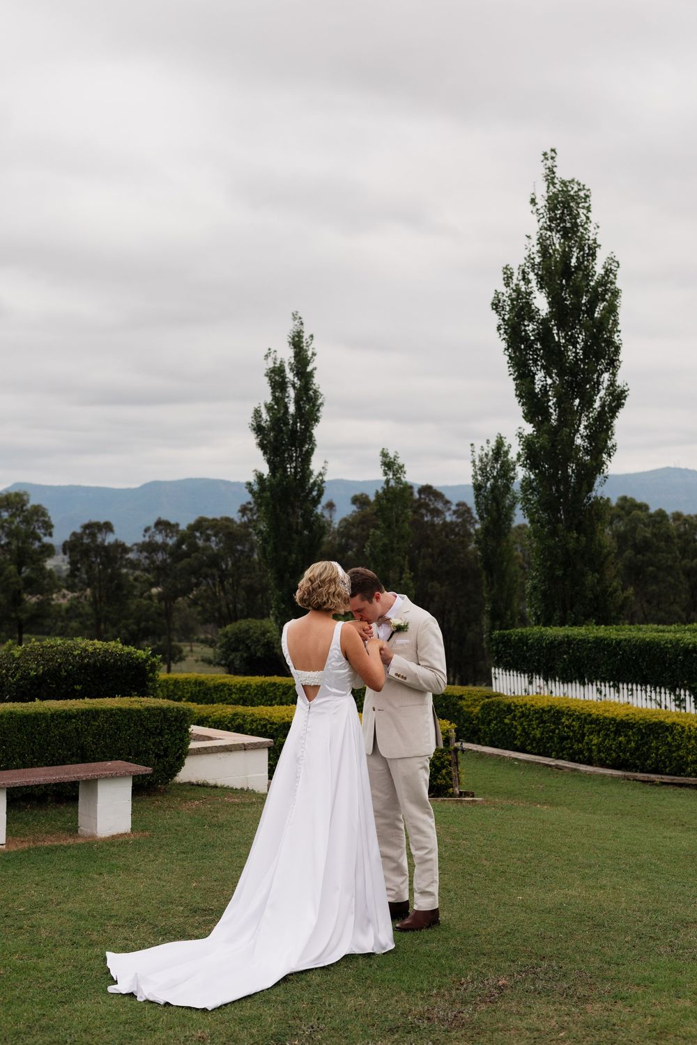 A couple shares an intimate moment on a scenic hilltop lawn overlooking mountains and gardens.