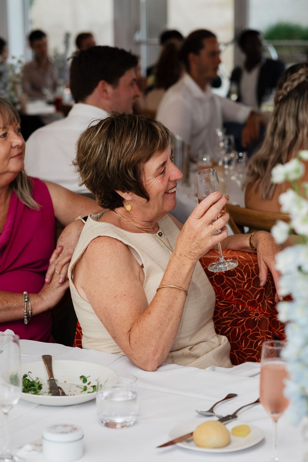 Wedding guests seated at elegant dining tables with white tablecloths and wine glasses at a reception.