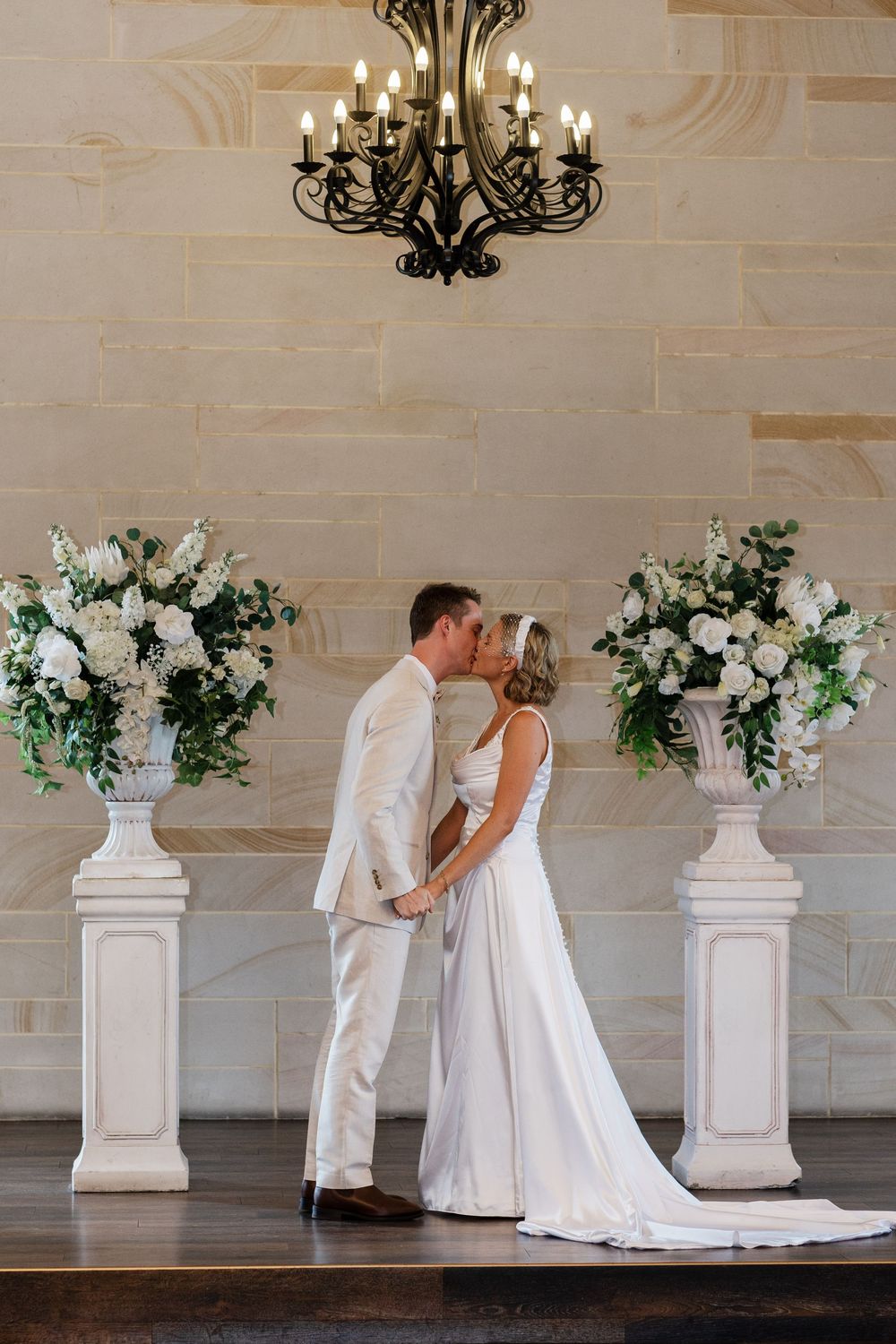 A romantic wedding sequence showing a couple in white attire posing against an elegant stone wall with floral arrangements.
