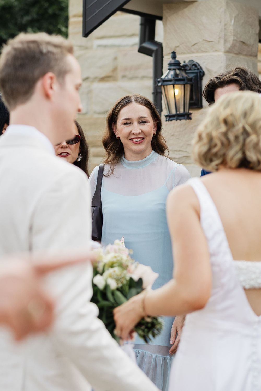 Wedding party members in light blue and white dresses share joyful moments during an outdoor celebration.