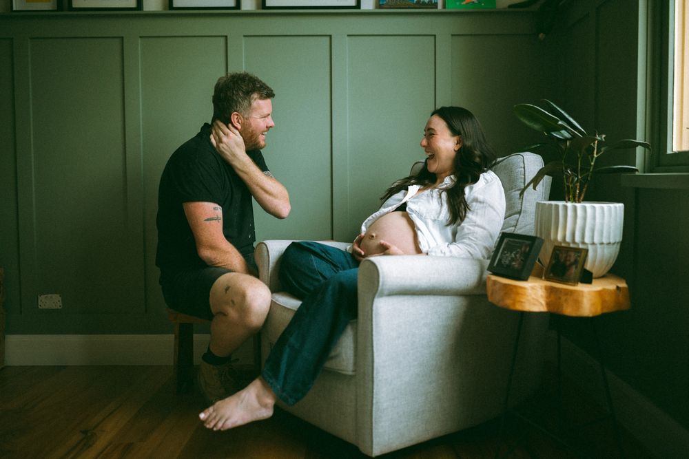 Two people sit on opposite ends of a white couch in a dark green room having a conversation.