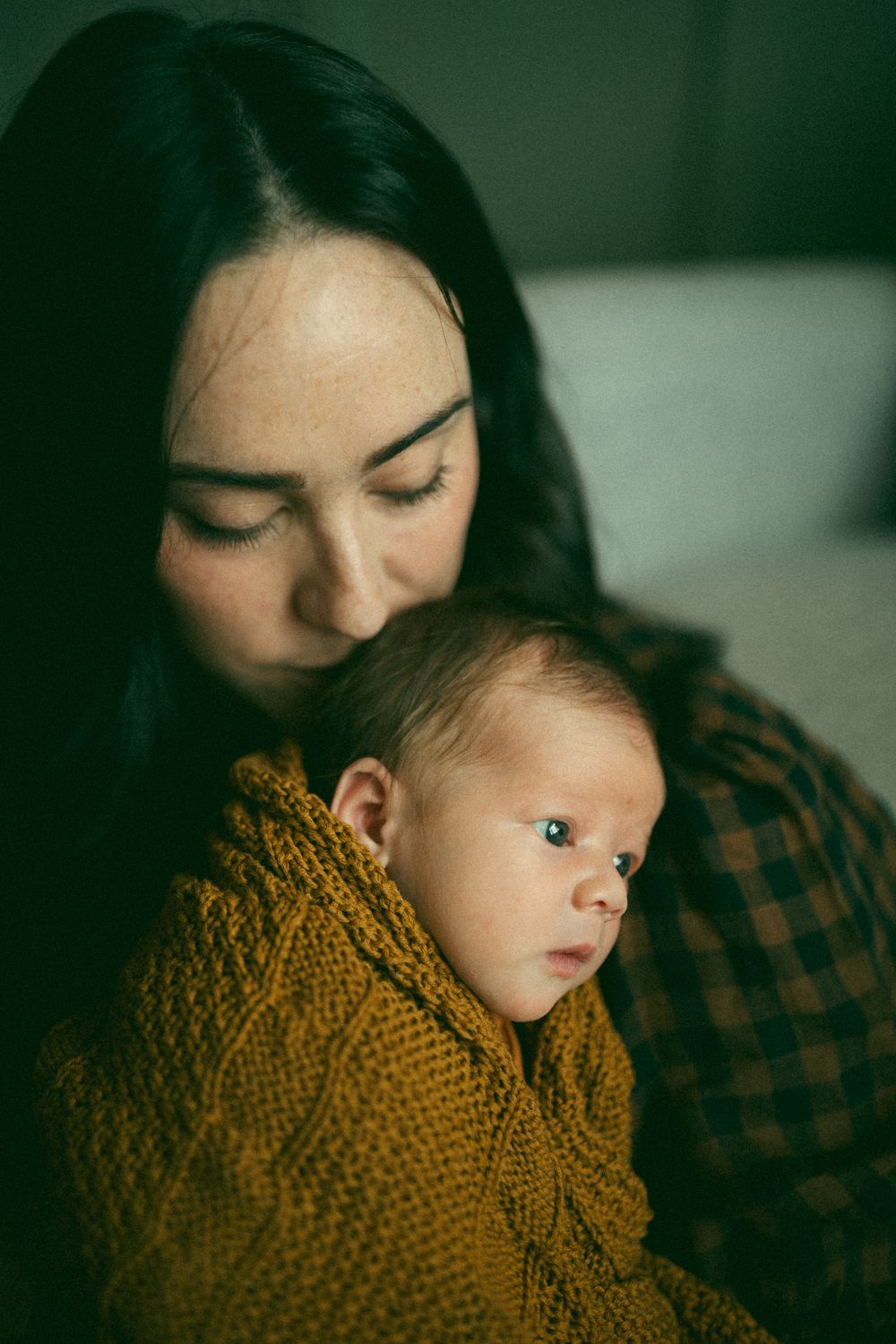 A series of intimate close-up shots showing a baby wearing a mustard yellow knit sweater in moody lighting.