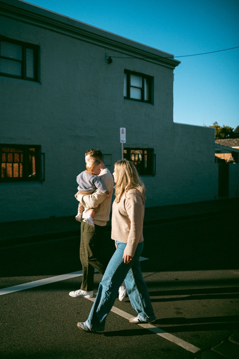 Four sequential photos show people walking along a sidewalk beside a white building in dramatic sunlight.