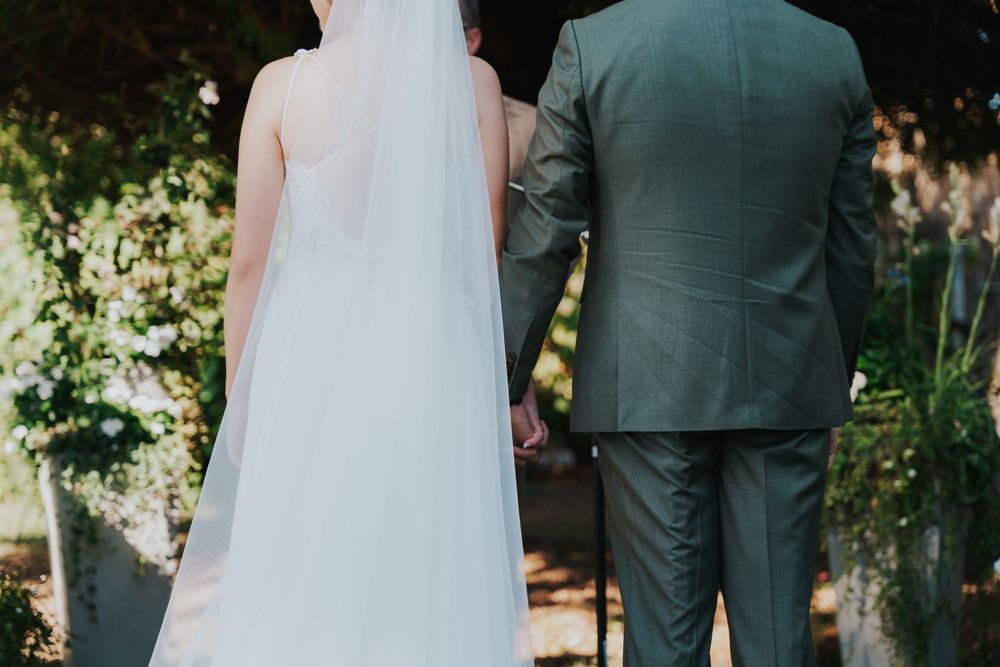 A couple in wedding attire stands together in a lush garden setting during their outdoor ceremony.