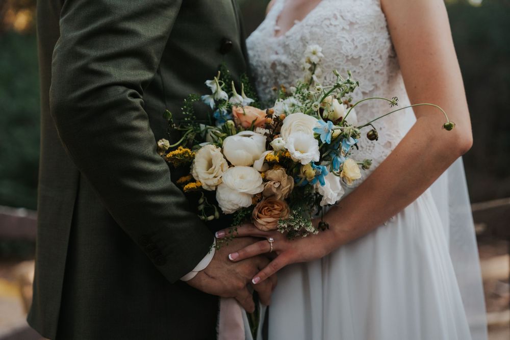 Wedding party members hold elegant bouquets with white roses and blue accents against formal attire.