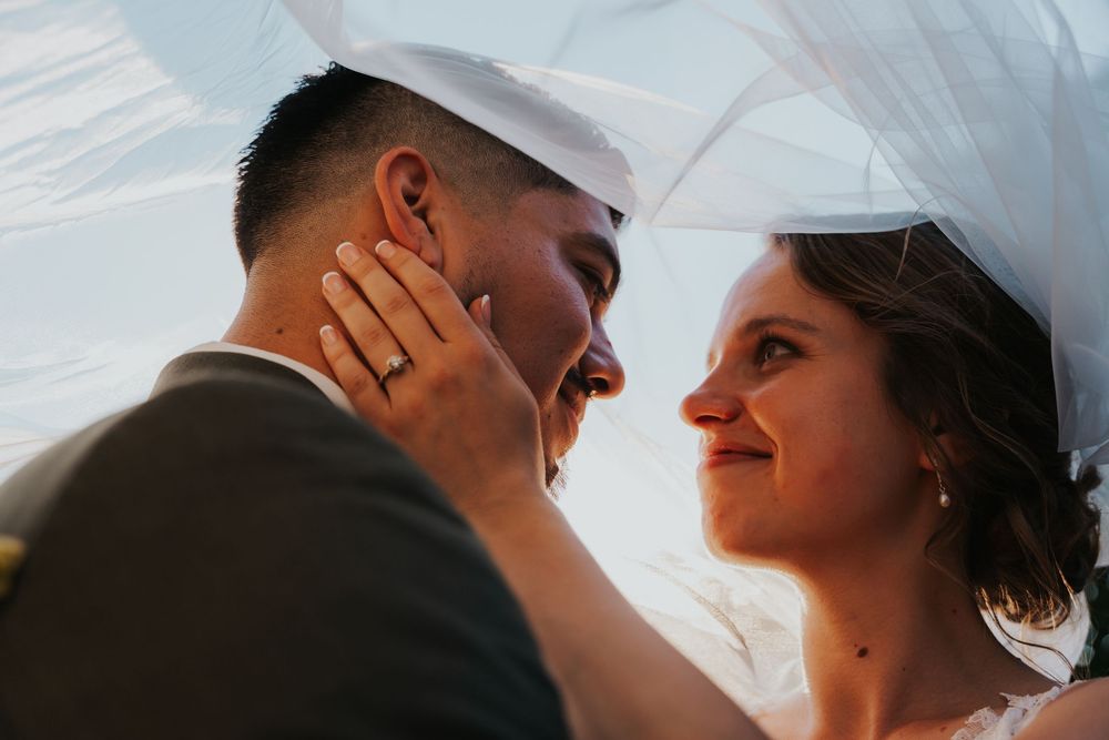 A romantic couple shares an intimate moment under a veil during their wedding day.