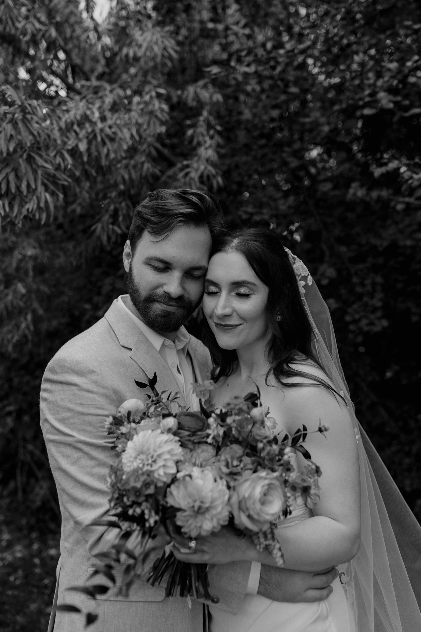 A joyful black and white wedding photo capturing a couple's intimate moment with floral bouquet.
