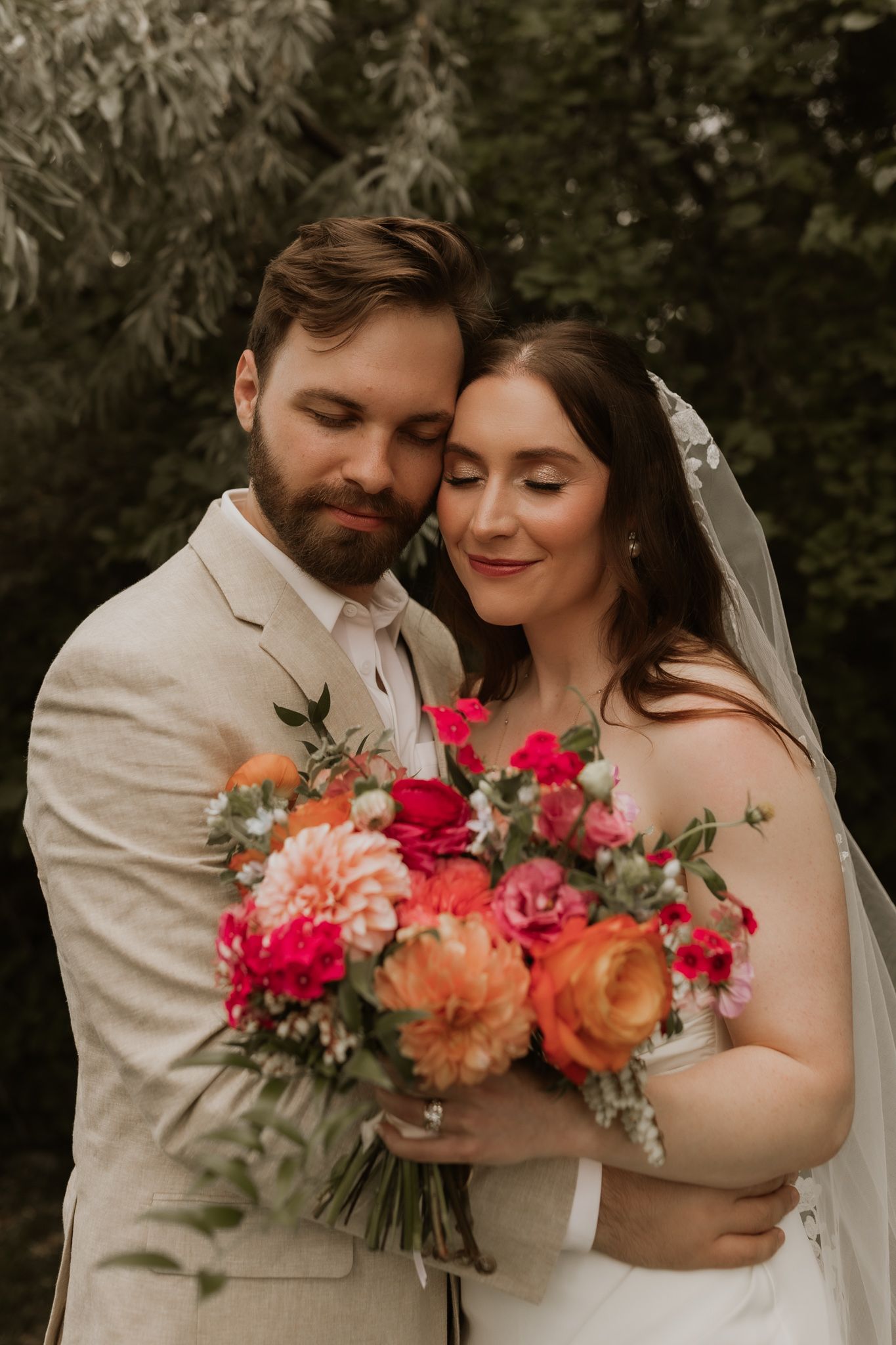 Intimate wedding portrait of a couple sharing a tender moment with a bright floral bouquet.