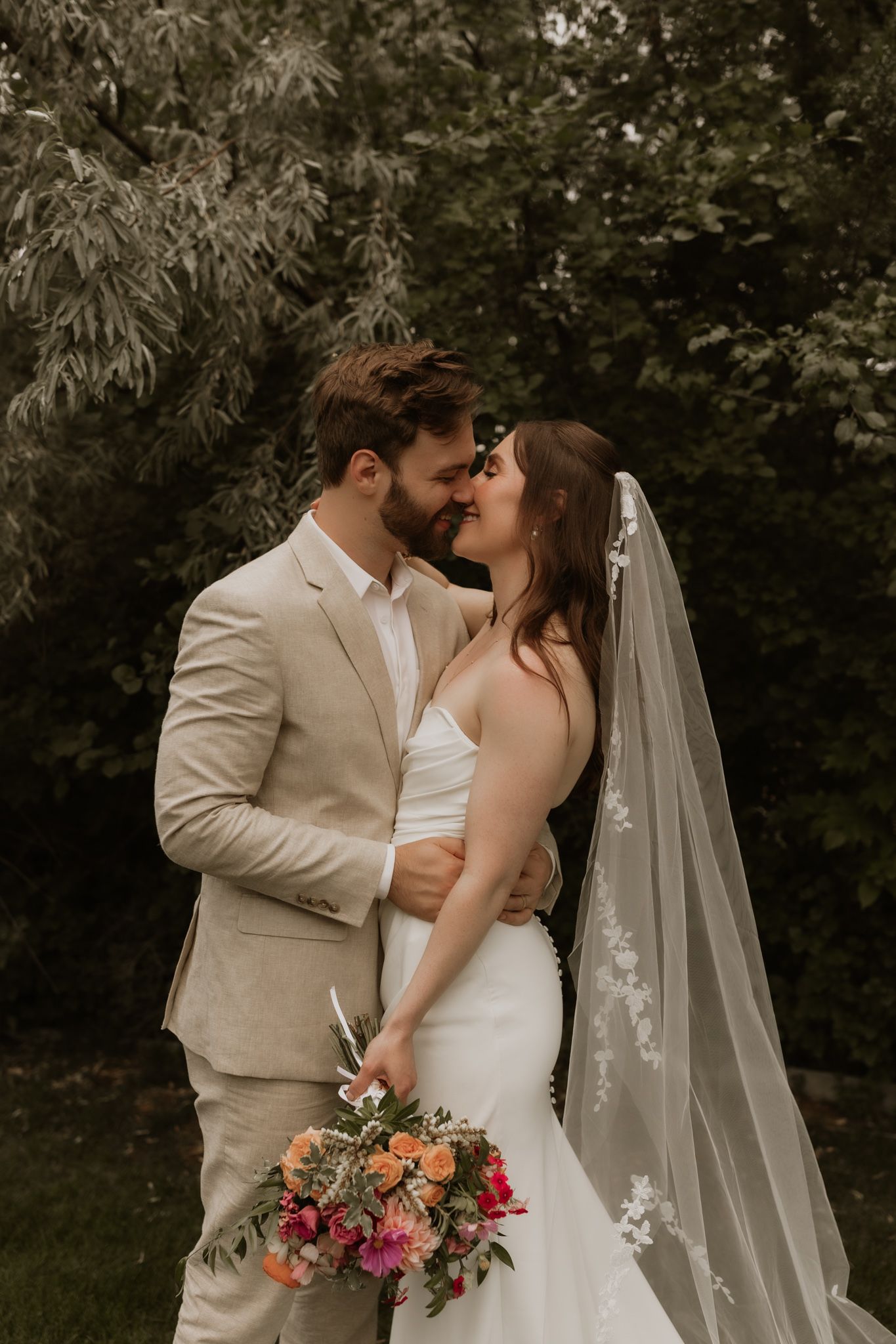 A tender wedding portrait featuring a couple sharing a romantic moment with coral and pink bouquet details.