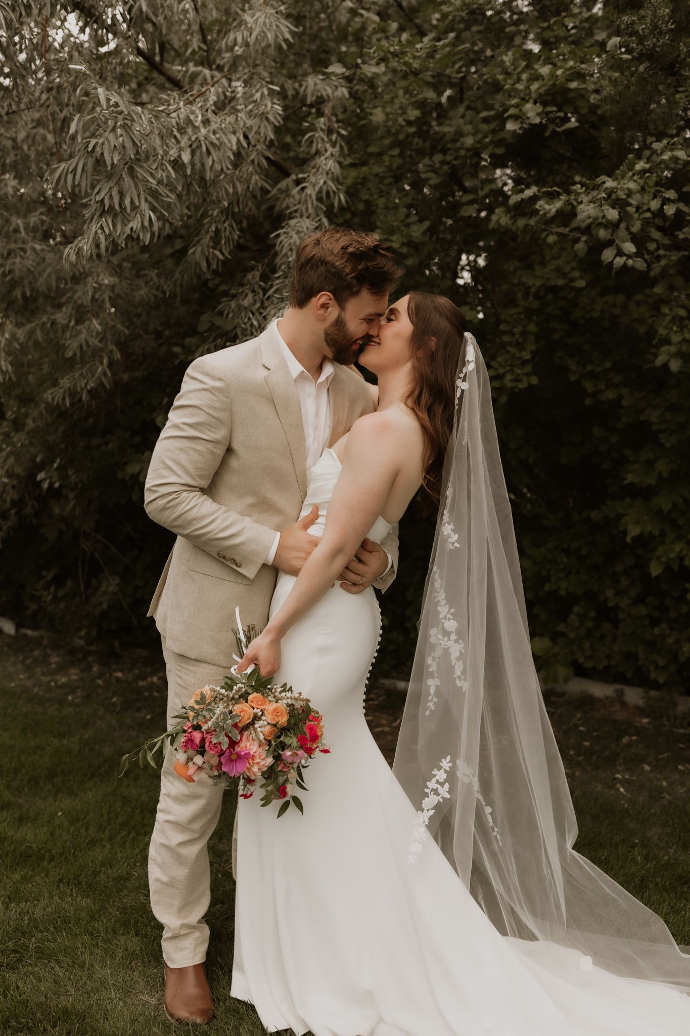 A romantic garden wedding photo with the couple sharing a kiss while holding a colorful bouquet.