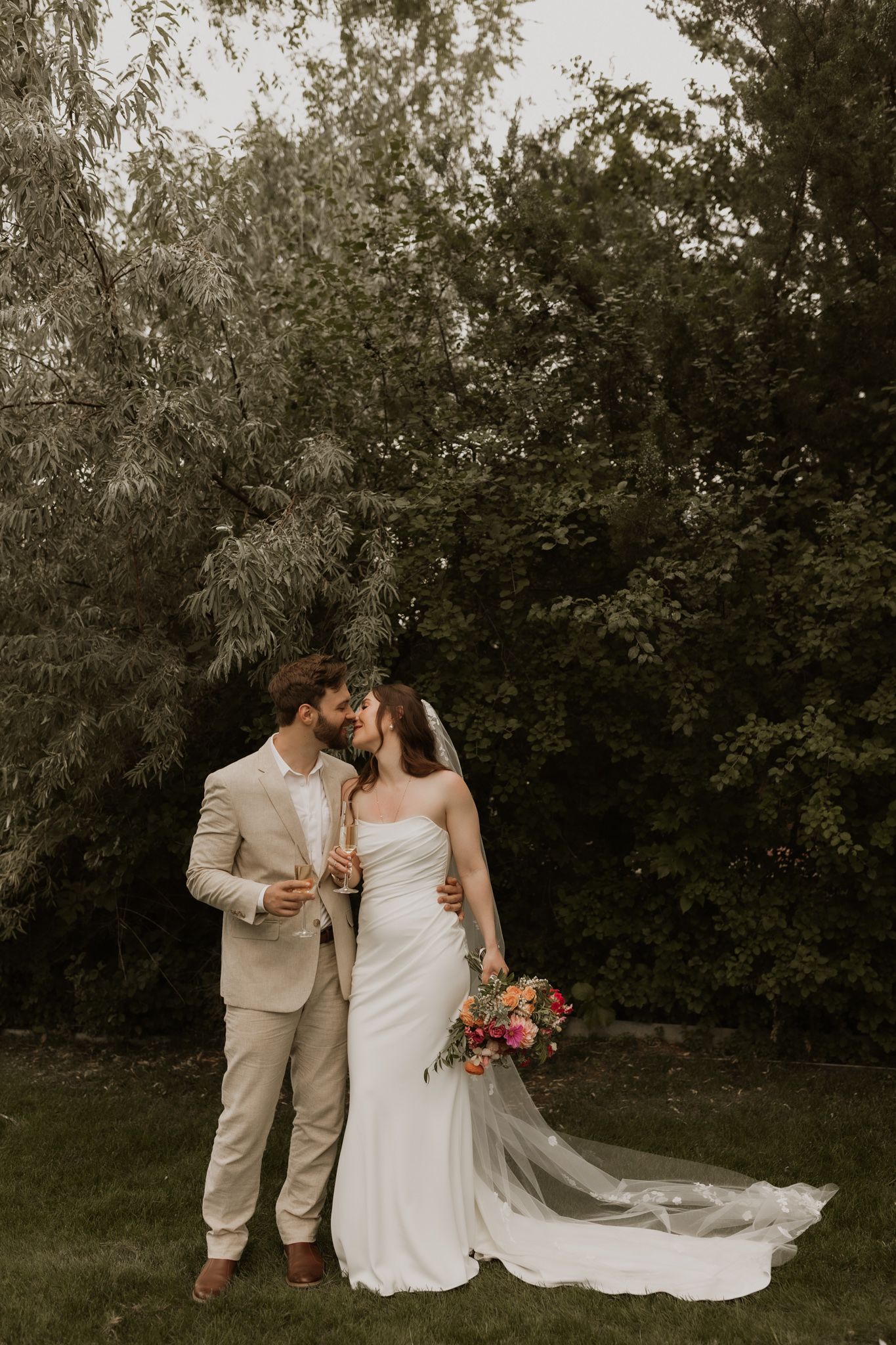 An intimate wedding portrait featuring a couple in light-colored attire with a flowing veil outdoors.