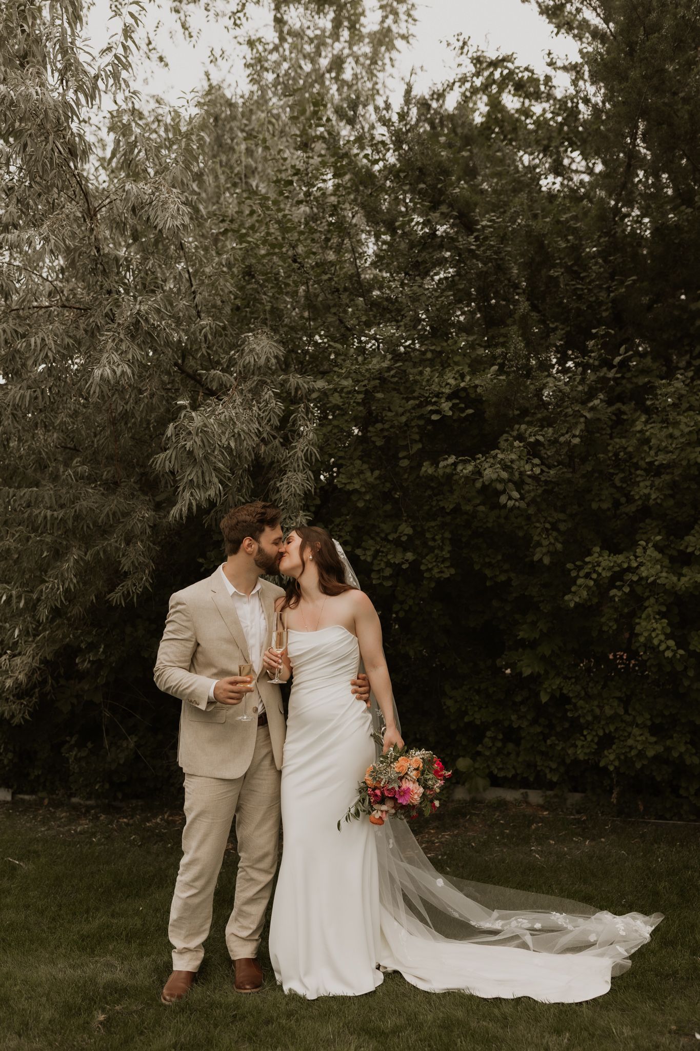 A romantic wedding couple shares an intimate moment in a garden setting with a flowing white dress and beige suit.