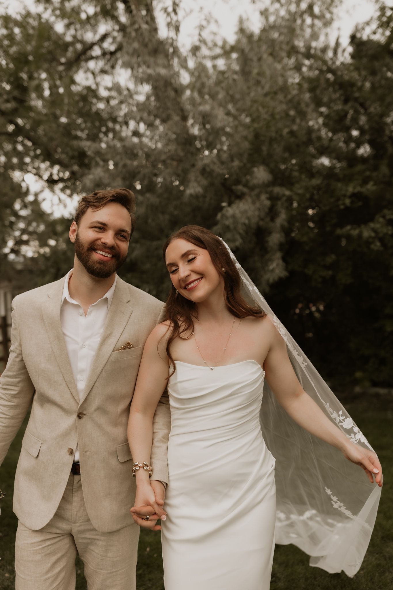 Newlywed couple in a garden setting wearing beige suit and white wedding dress sharing romantic candid moments.
