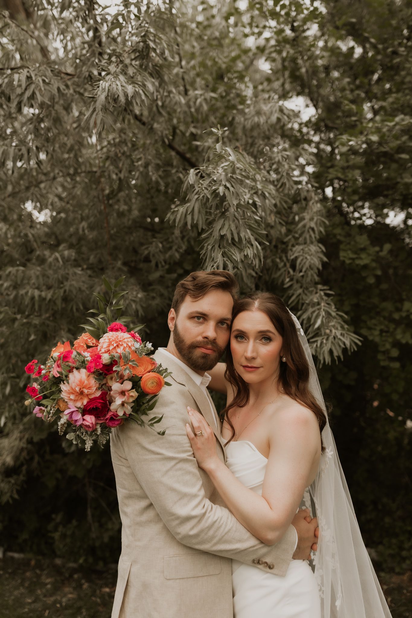 An elegant outdoor wedding photo with a couple in beige and white against a natural garden backdrop.