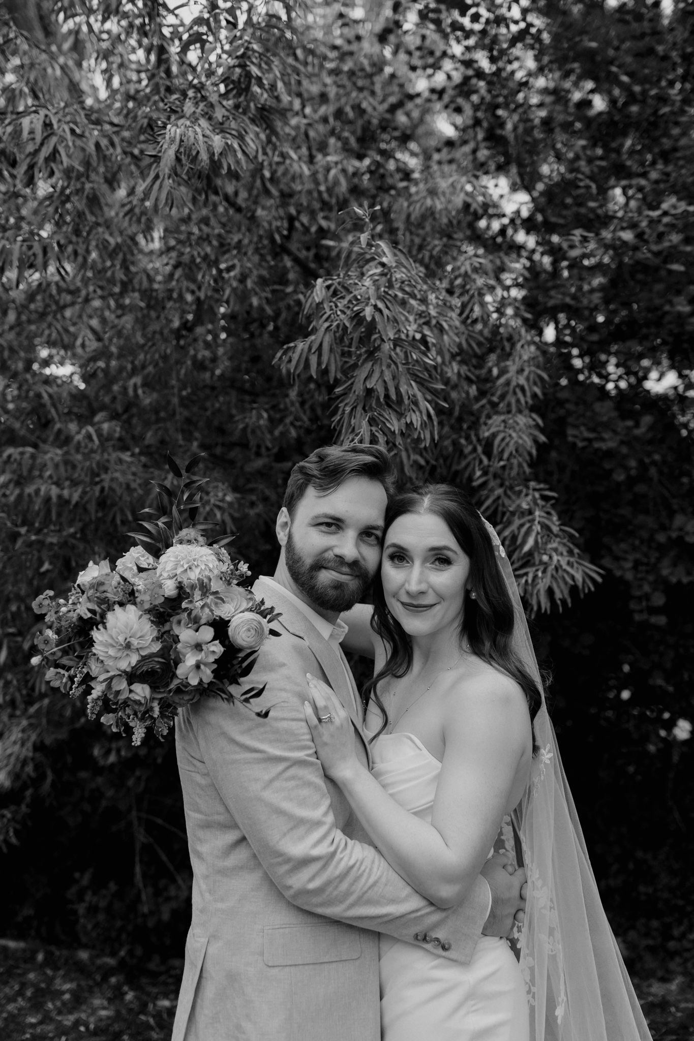 Candid wedding photo capturing couple's laughter in natural outdoor setting.