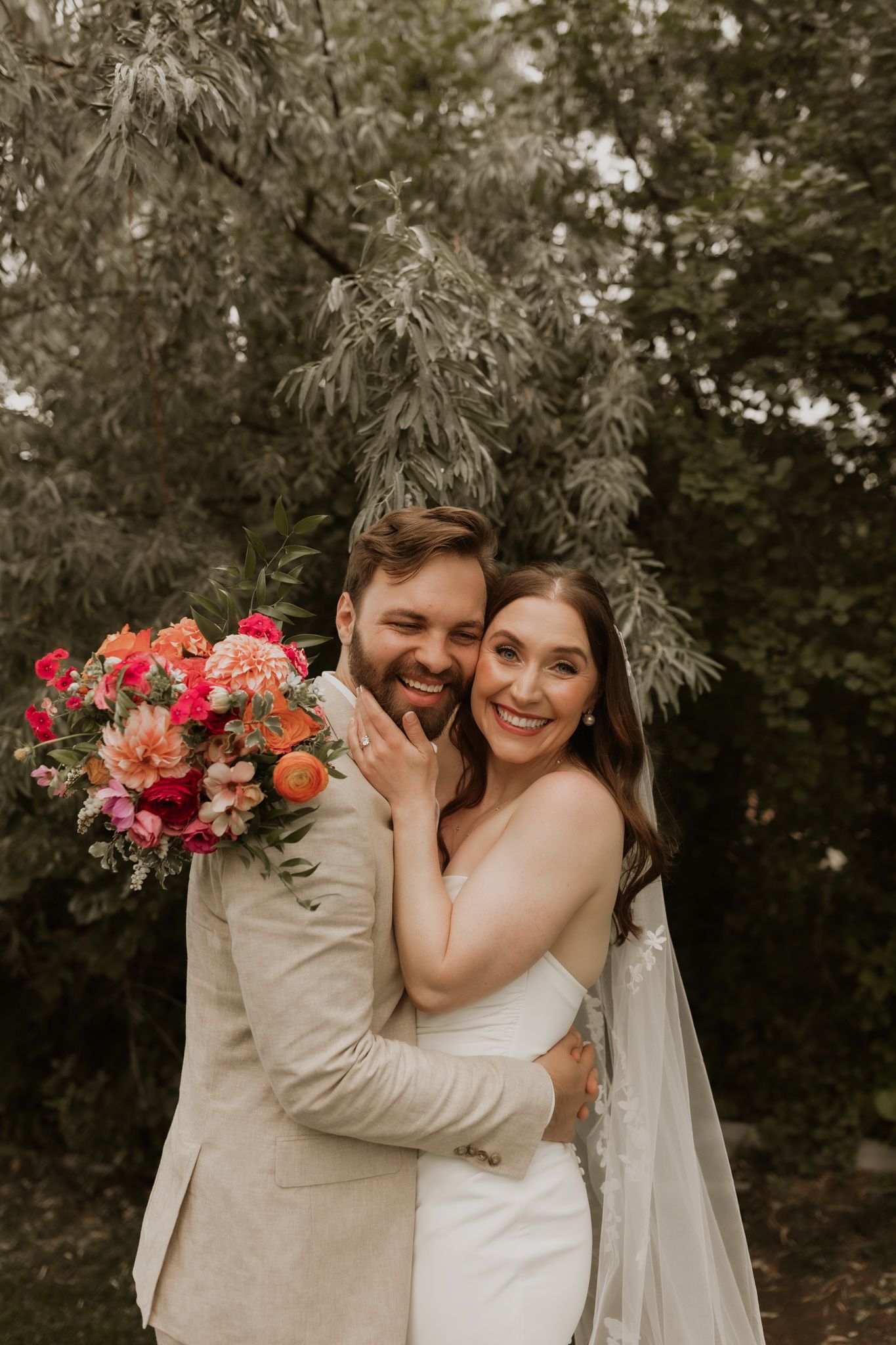A romantic moment between newlyweds sharing laughter in a garden setting with a colorful floral bouquet.