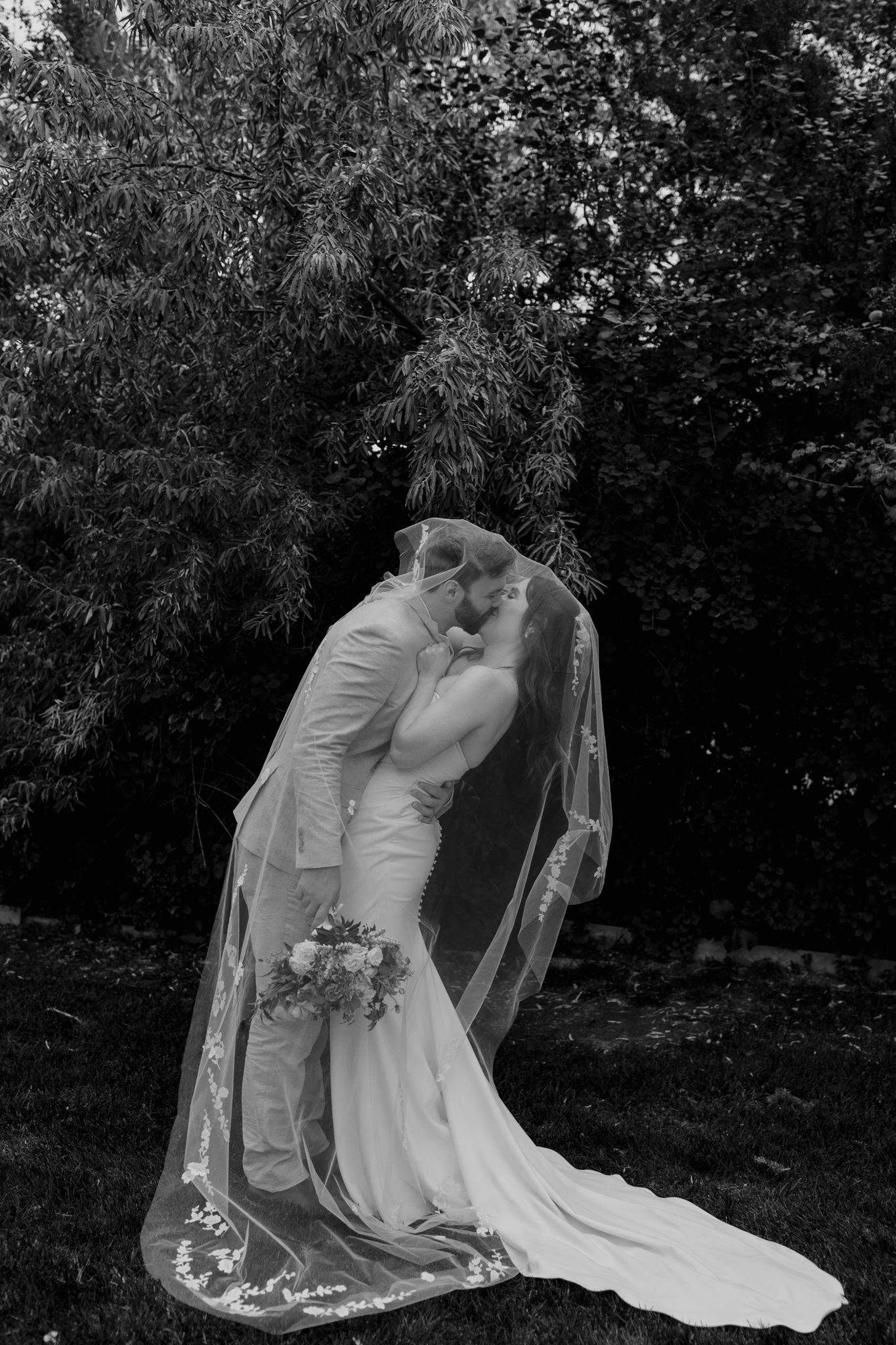 A romantic black and white wedding photo series showing a couple embracing in a garden setting with flowing veil and dress details.