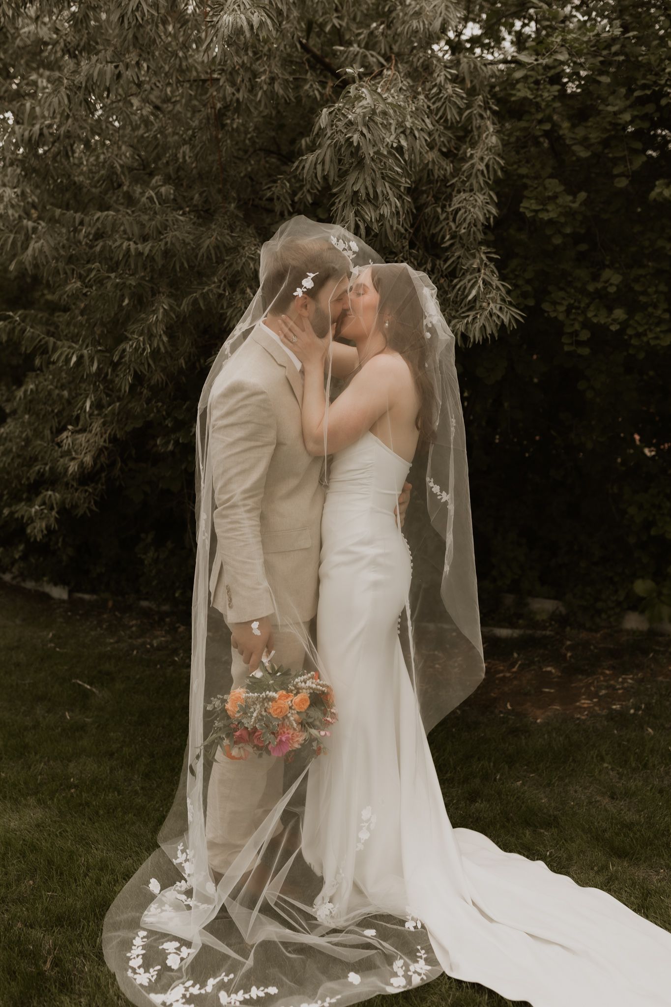 A romantic wedding portrait showing a couple kissing under an elegant lace veil.