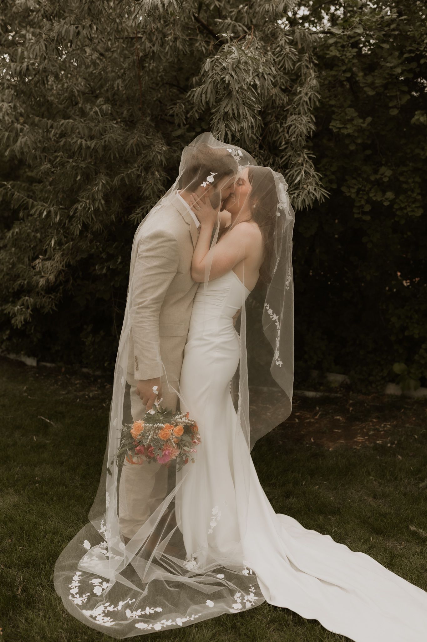 An artistic wedding portrait featuring a flowing veil and intimate embrace in natural lighting.