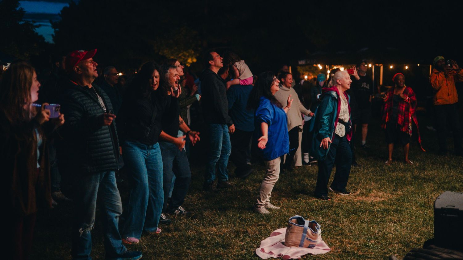 A crowd of people gather outdoors at night with glowing lights and lanterns creating a festive atmosphere.