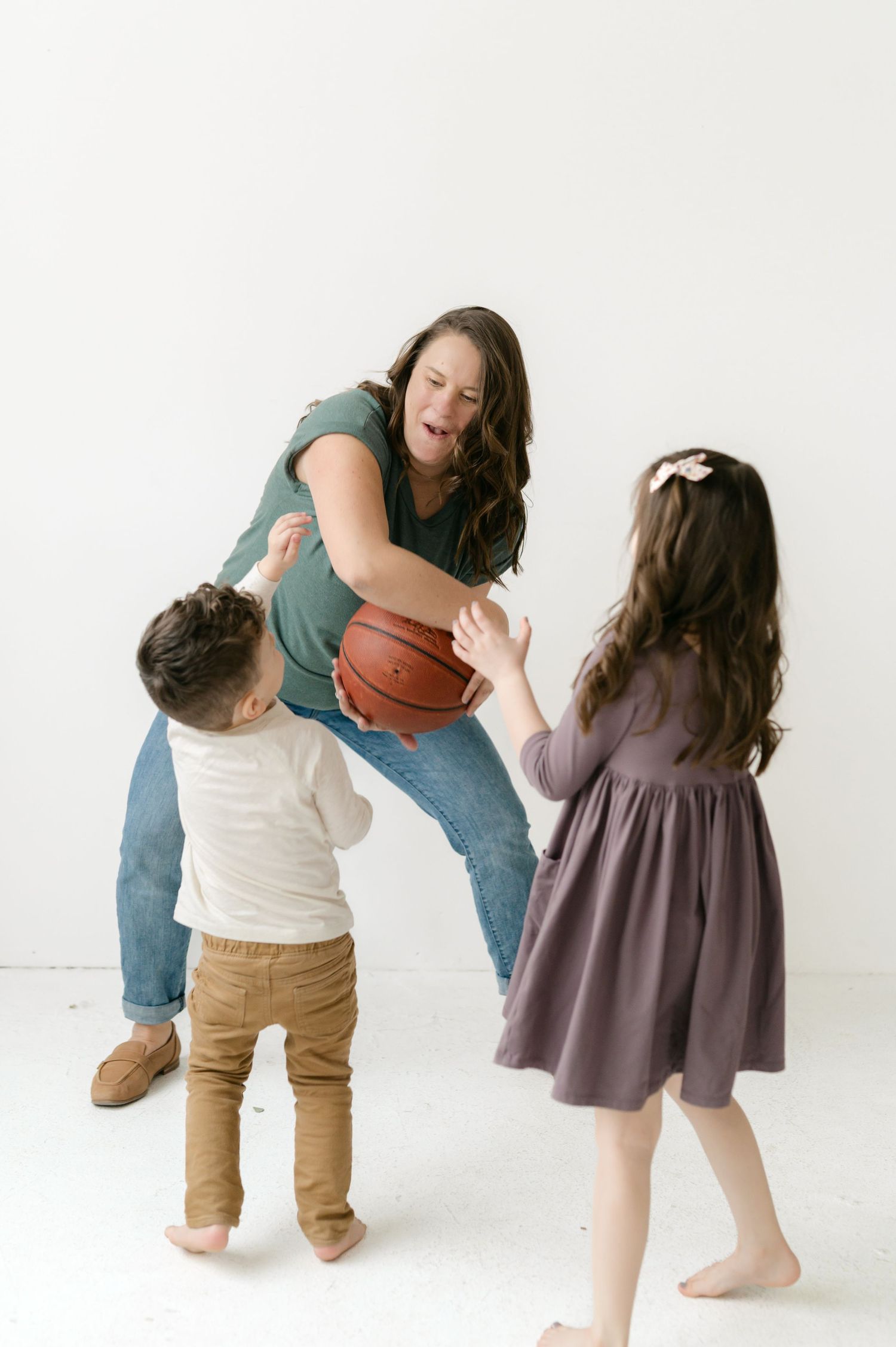 Two children play together with a basketball in a minimalist white studio setting.