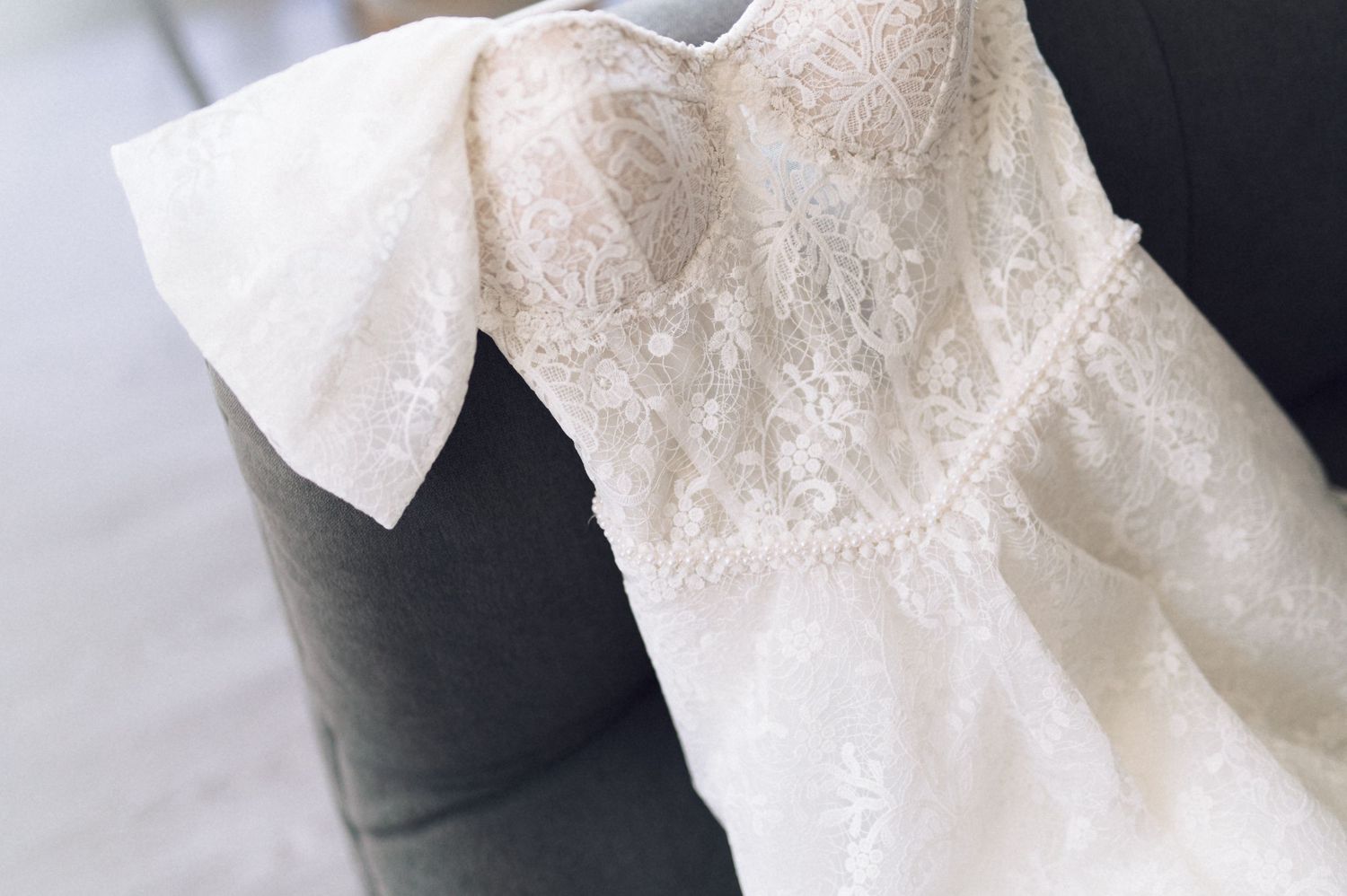 Close-up detail of delicate white lace and bow on a wedding dress against dark background.