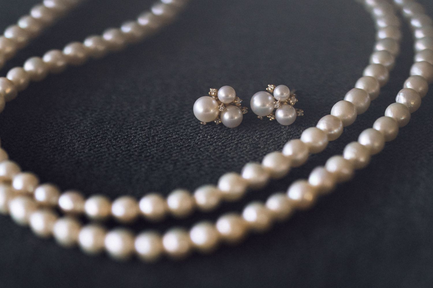Elegant pearl necklace and matching stud earrings displayed on dark background with soft focus.