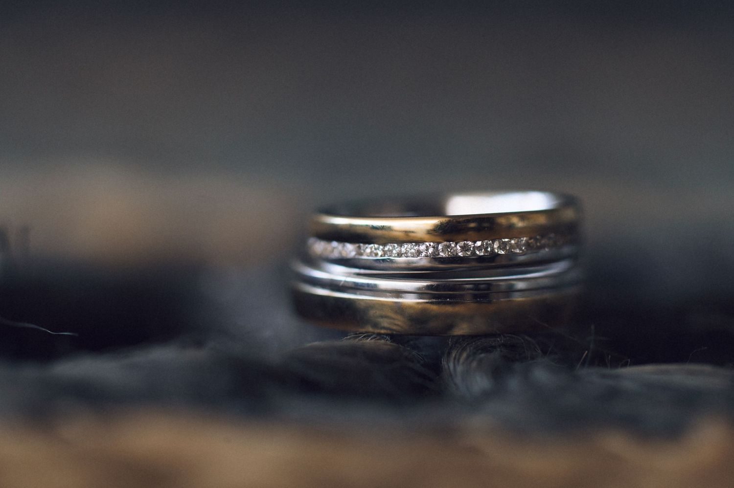 A close-up macro shot of two wedding rings with diamonds on a dark reflective surface.