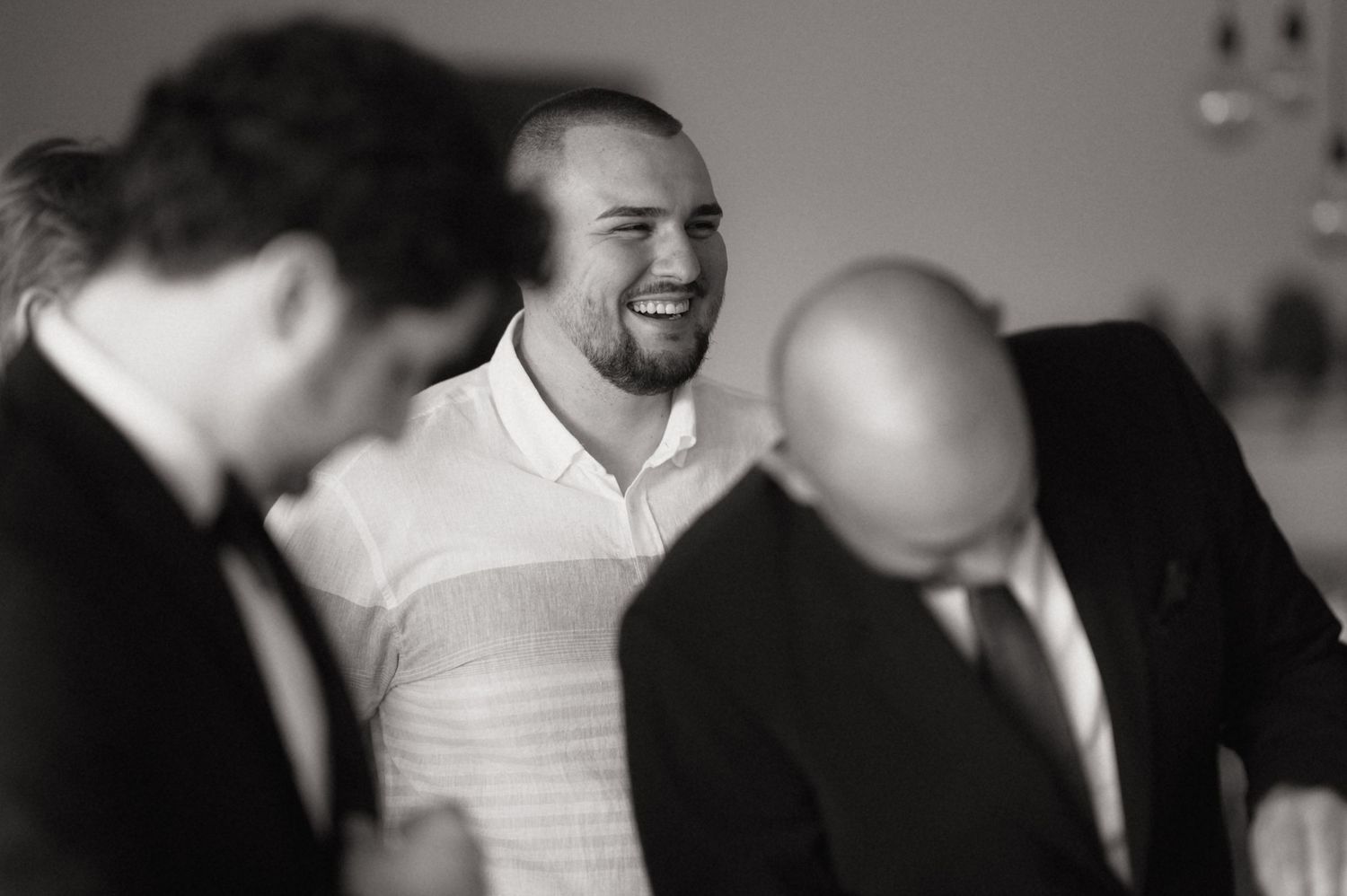 Black and white candid photo showing three men in conversation at a social gathering, with one wearing a white shirt.