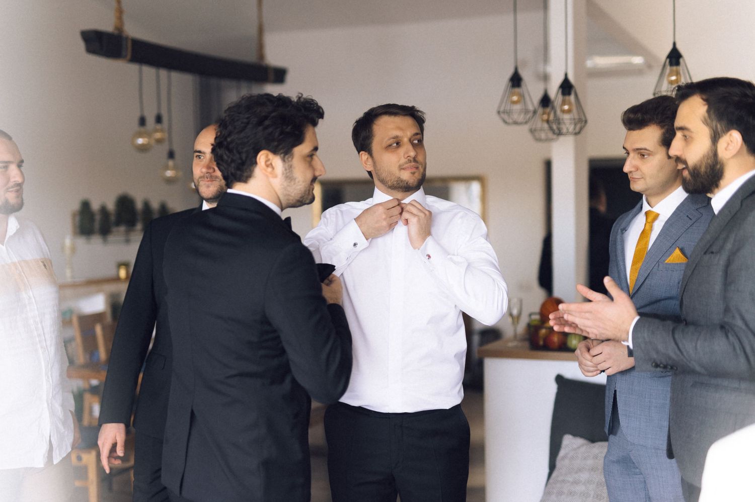 A group of well-dressed men in suits and formal attire gather for conversation at an indoor event.