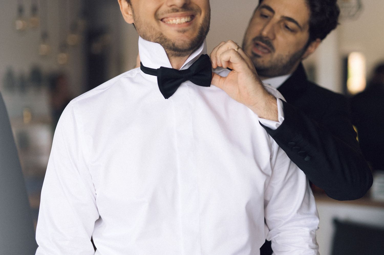 Restaurant servers in white shirts and black bow ties carry plates of food through an elegant dining room.