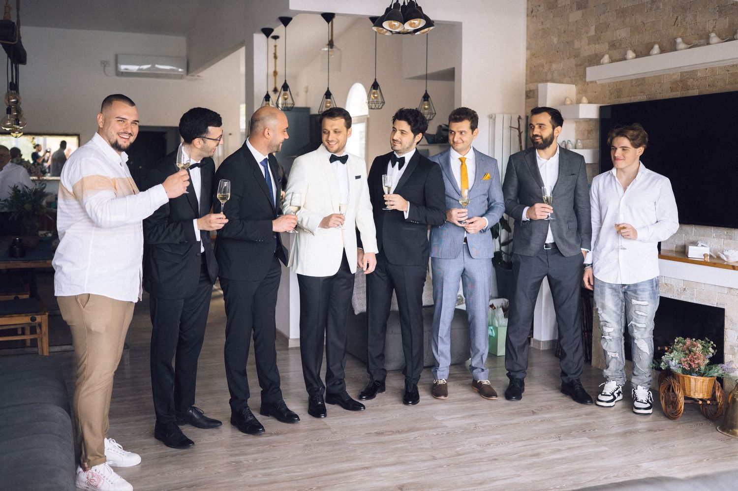 A group of well-dressed guests in formal attire gather at an elegant indoor event space with pendant lighting.