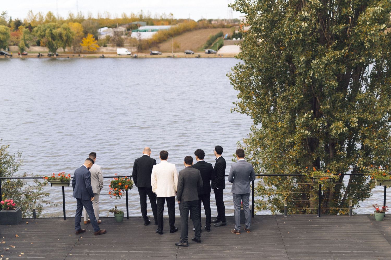 A group of people gather by a scenic lake surrounded by autumn trees and foliage during an outdoor event.